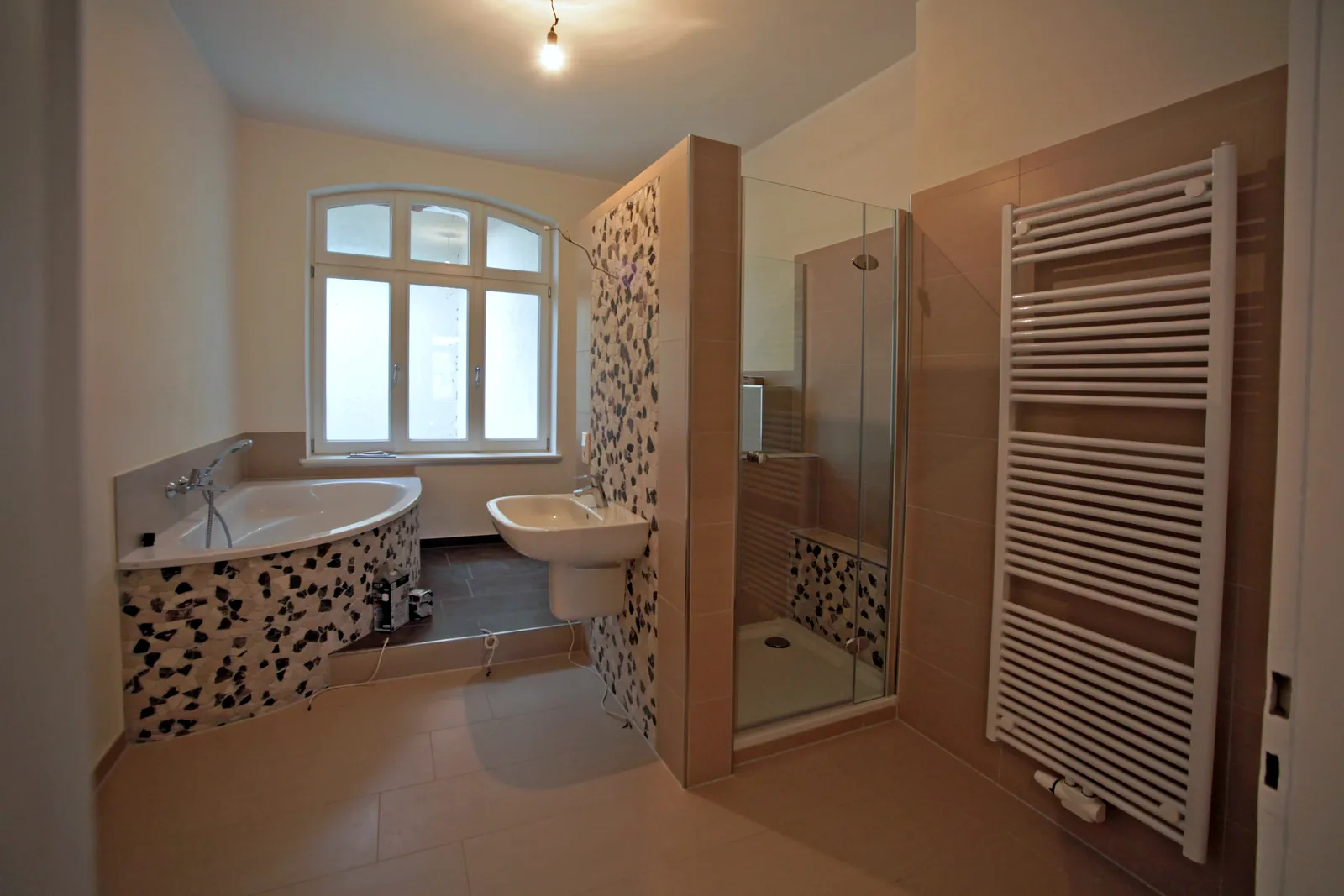 Modernes Tageslichtbad der Villa Valentino mit Eckwanne, Natursteinmosaik und bodengleicher Dusche