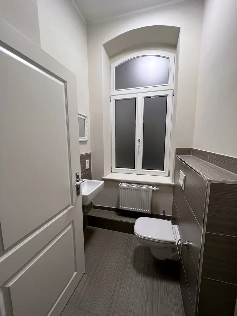 Gäste-WC der Villa Valentino mit dunklen Wandfliesen, wandhängendem WC und Rundbogenfenster